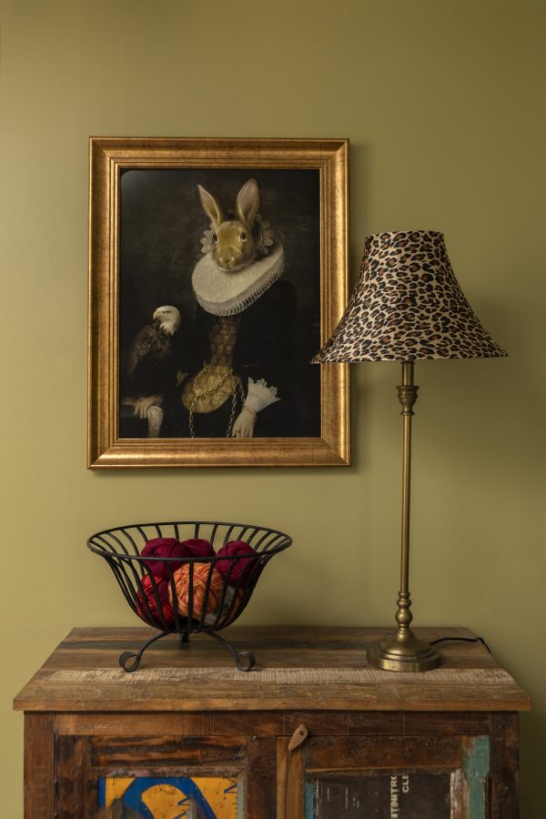 Leopardikuvioinen pöytävalaisin ja lankakori sivupöydällä. Seinällä taulu.