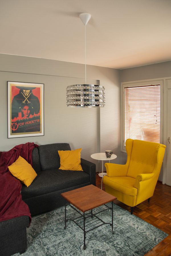 Olohuoneen sisustus jossa kromin värinen kattovalaisin Mirka-38, harmaa sohva, keltainen nojatuoli, kaksi pöytää, taulu ja matto.