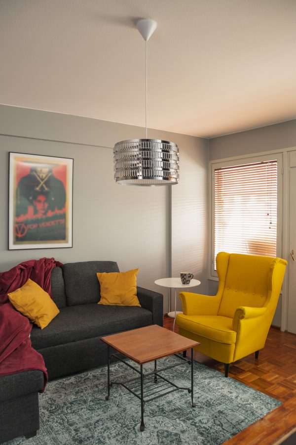Olohuoneen sisustus jossa kromin värinen Moona-38 kattovalaisin, harmaa sohva, keltainen nojatuoli, taulu, kaksi pöytää ja matto.