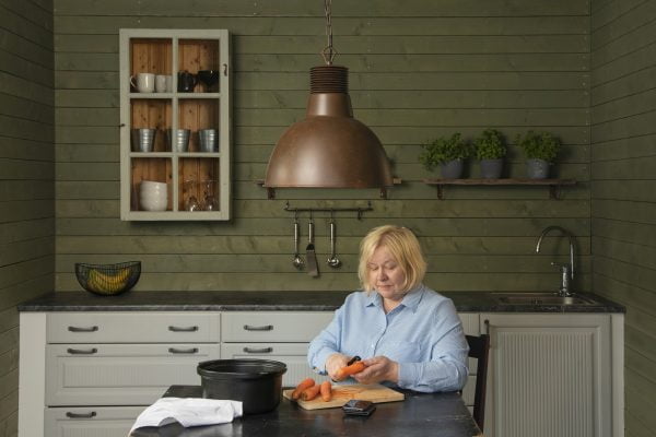 keittiön sisustus, jossa ruskea Patricia riippuvalaisin, kaappi ja hylly seinällä. Nainen istuu pöydän ääressä ja kuorii porkkanoita.