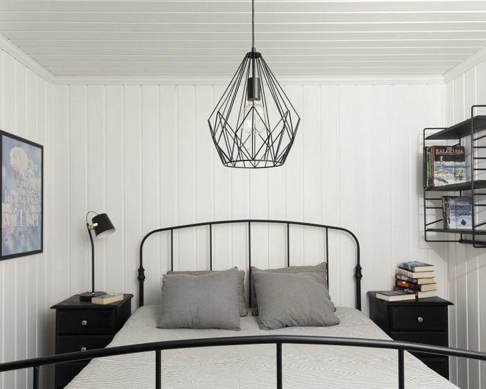 Makuuhuoneen sisustus, jossa musta metallilangasta tehty kattovalaisin ja musta pöytälamppu yöpöydällä