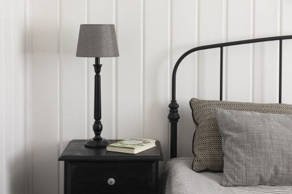 Makuuhuoneen sisustus, jossa on yöpöydällä musta Hampshire pöytävalaisin ja harmaa Åsa-20 varjostin. Sängyllä on koristetyynyjä.