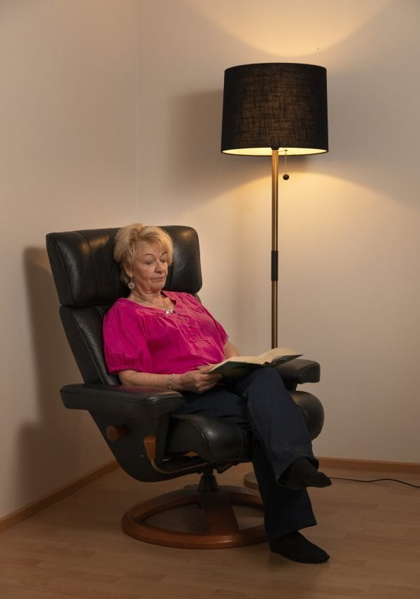 Olohuoneen sisustus, jossa lukunurkka.Tilan lukuvalo on antikmessingin värinen Stockholm-L lattiavalaisin, mustalla tuolilla istuu nainen lukemassa.
