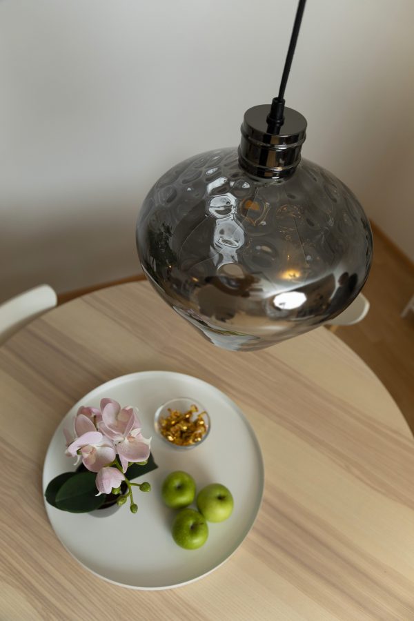 Keittiön sisustus, jossa vaalean pyöreän ruokapöydän päällä on kromin värinen lasinen Fenix riippuvalaisin.