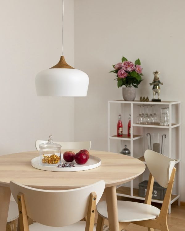 Keittiön sisustus, jossa metallinen valkoinen riippuva kattovalaisin vaalean pyöreän pöydän päällä. Valaisimen yläosassa puukuvioitu koristeosa.