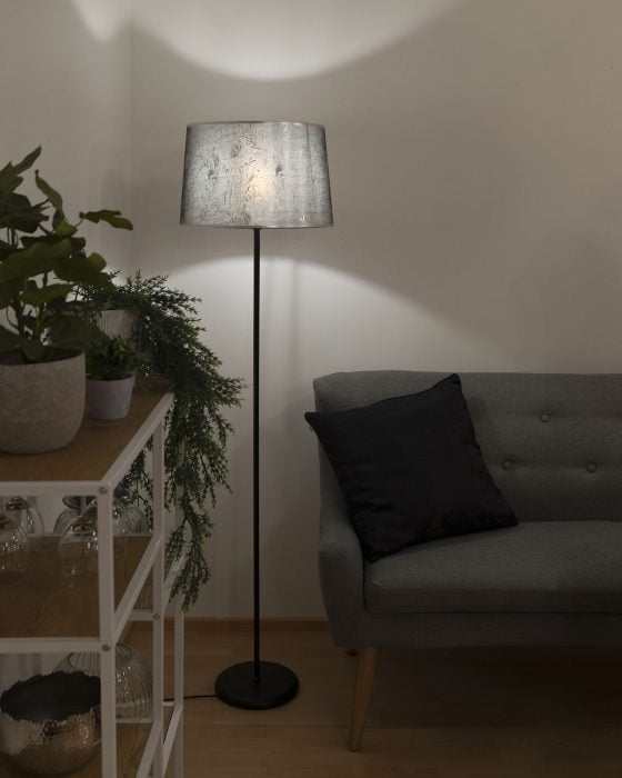 Mustan ja hopean sävyinen varjostin mustassa lattiavalaisimessa sohvan vieressä.