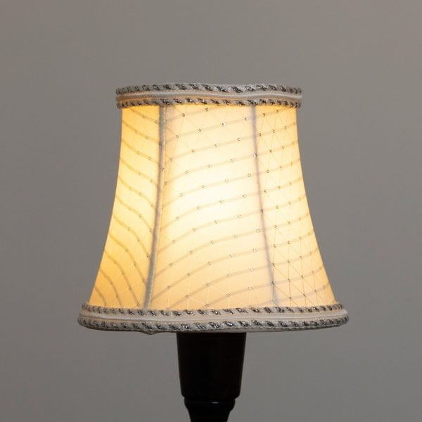 Kerman värinen lampunvarjostin, jossa hopean sävyinen koristenauha reunoissa.